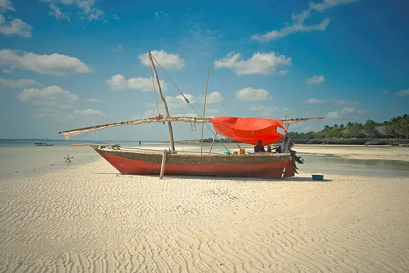 Traditional dhow boat with red sail on a sunny Zanzibar beach in Tanzania.