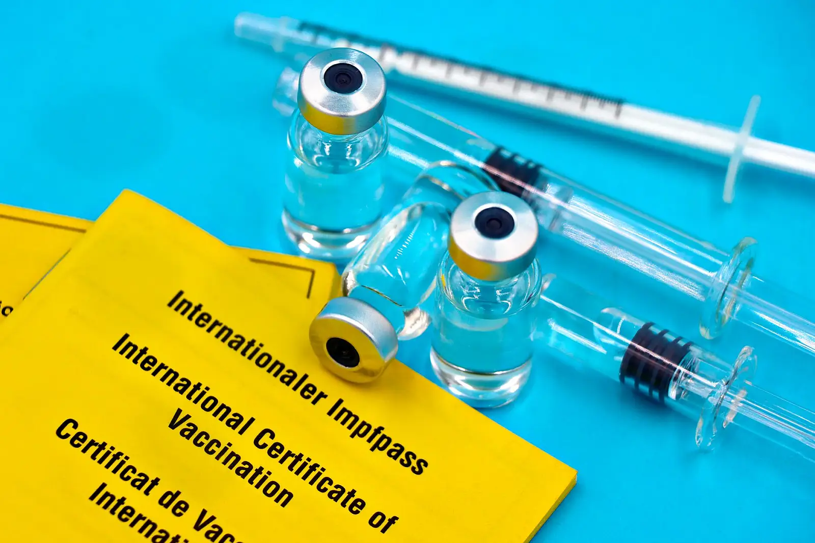 Close-up of vaccine vials, syringes, and international vaccination certificates on a blue surface.