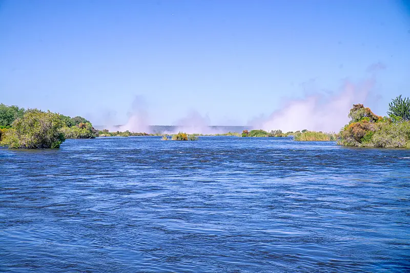 Beautiful river scene with mist, vibrant greenery, and clear blue sky.